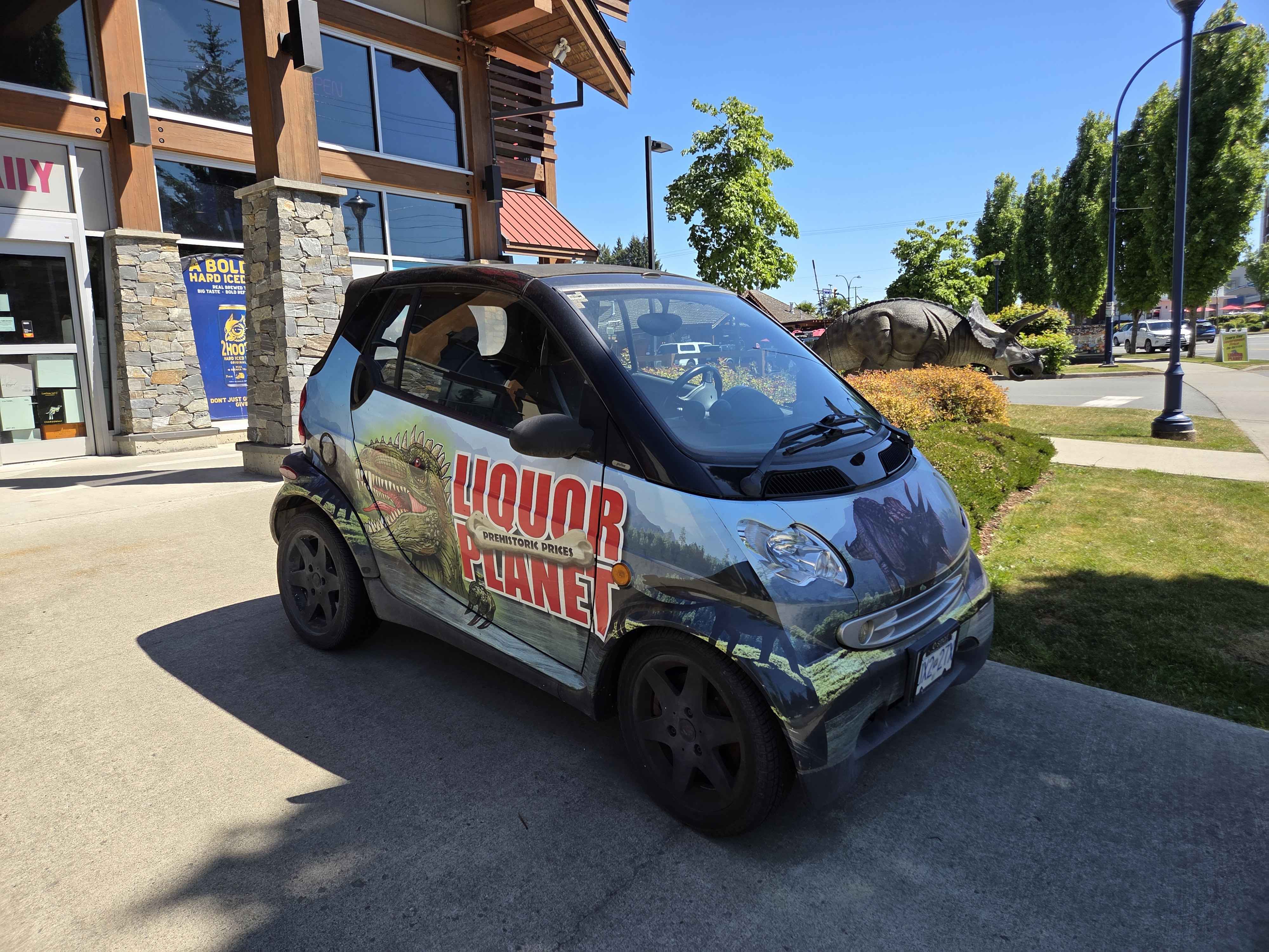 A Smart car wrapped in the Liquor Planet livery with a T-Rex and the Liquor Planet logo painted on it