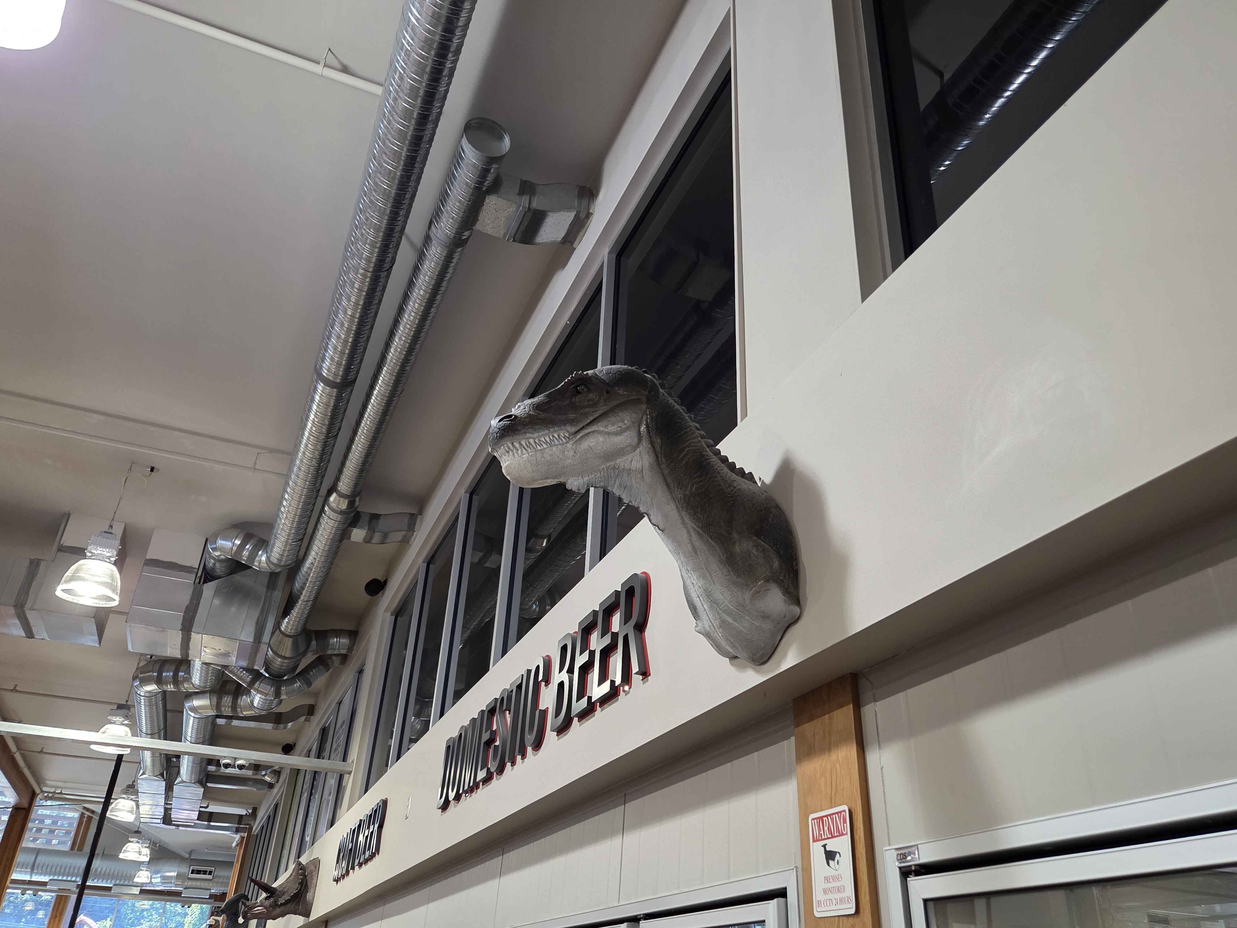 A long-necked sauropod head peeking out of the wall above the Domestic Beer section