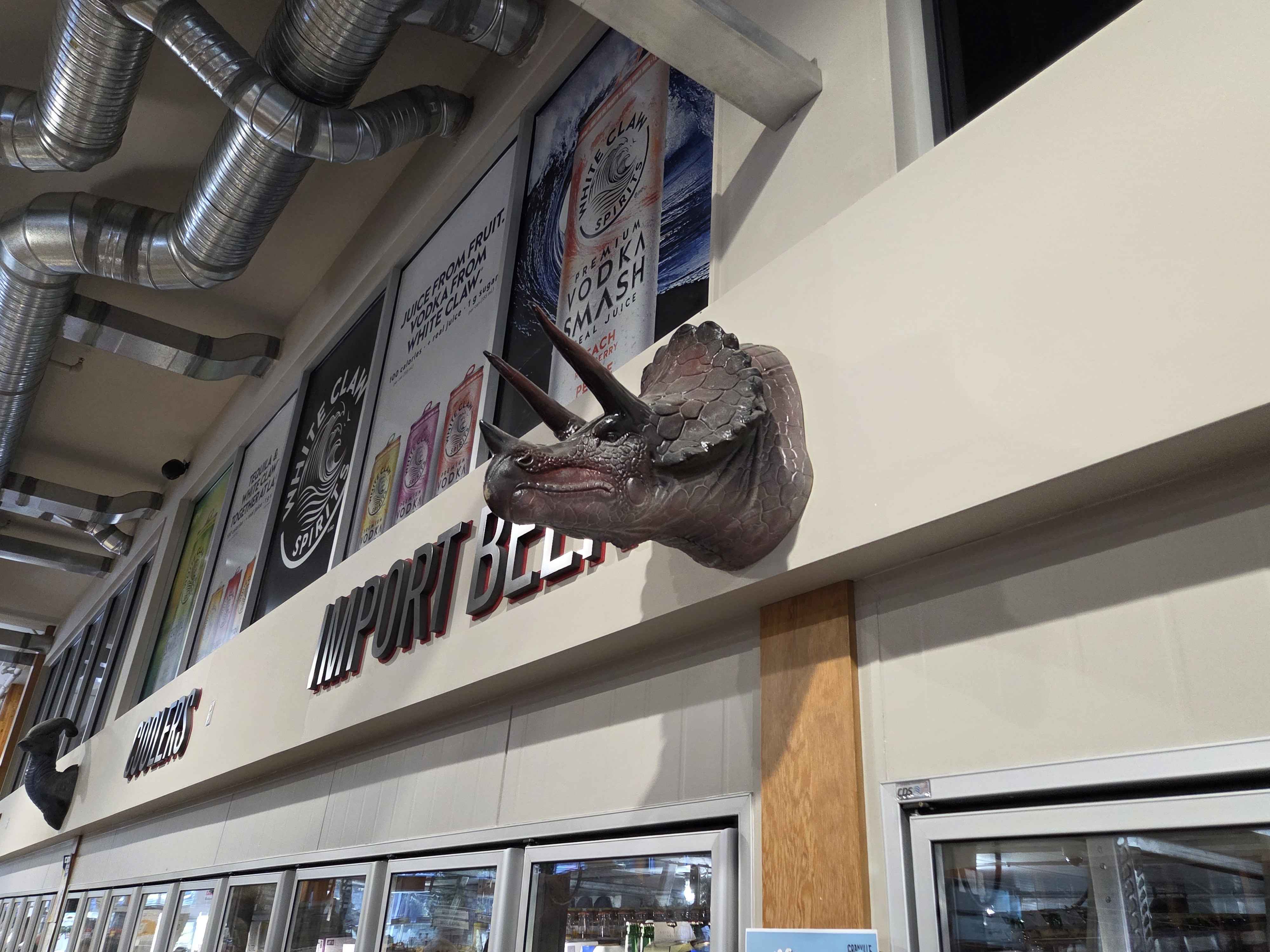 A horned Triceratops bust mounted on the wall above the Import Beer section