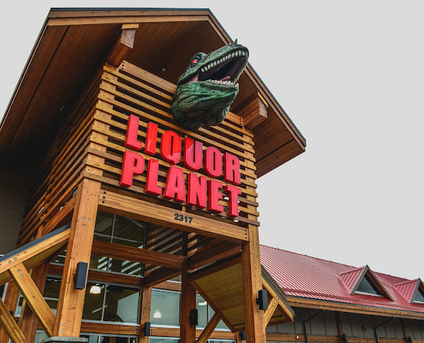 Liquor Planet storefront, angled view showing the giant T-Rex head over the entrance with the LIQUOR PLANET sign